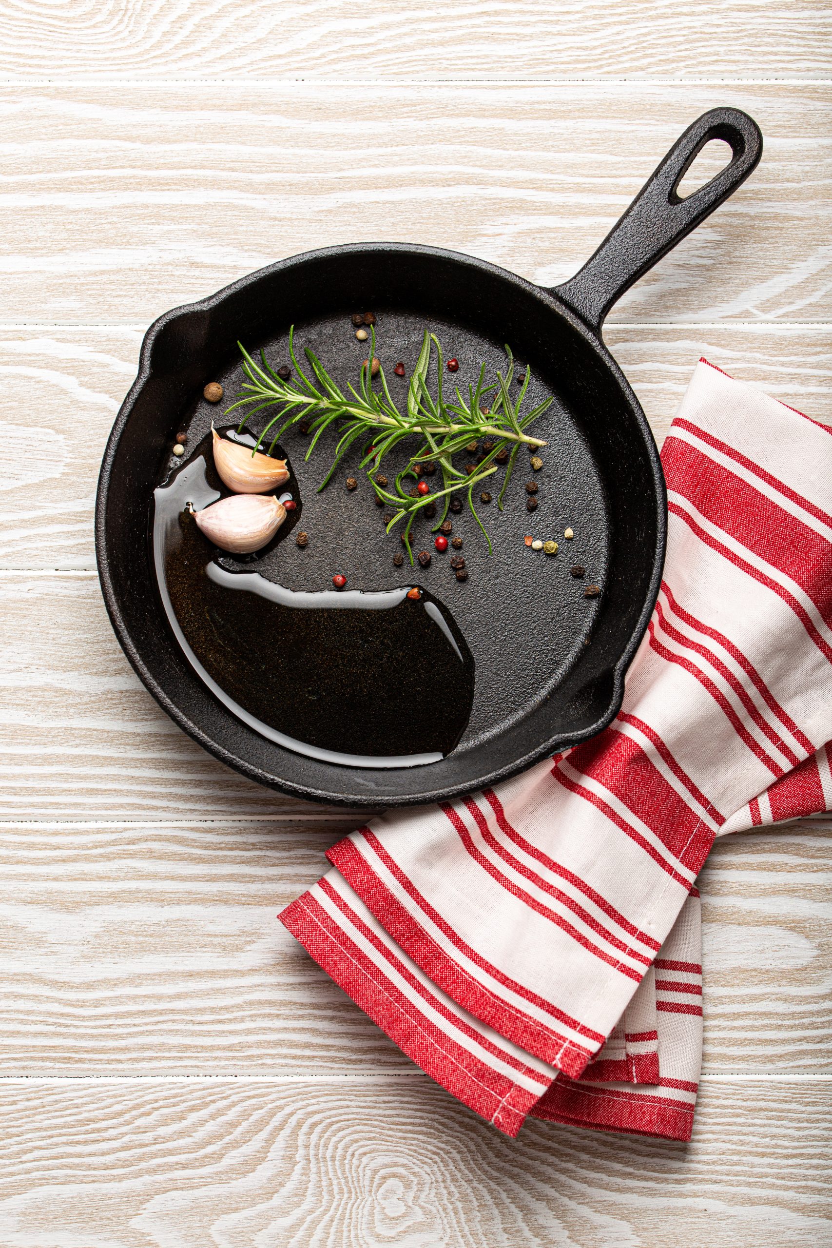 Black cast iron frying pan with rosemary, garlic, pepper, oil Black cast iron frying pan with rosemary, garlic, pepper, oil